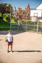 Basketball player looking at camera holding the ball under his arm in a street basketball court 