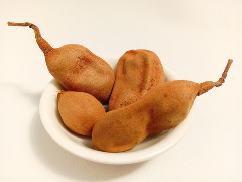 Tamarindus indica or tamarind is a sour-tasting fruit with a white background.