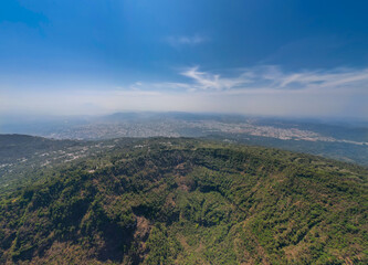 Aerial drone shot panorama of San Salvador volcano crater, National Park and The capital city of El Salvador in the background. Sunny day, blue sky.