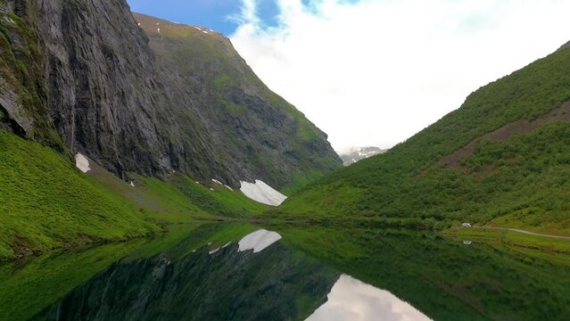 Norweigan Fjords Stavbergvatnet Urke, In the heart of a valley, a lake encircled by towering mountains, creating a serene and picturesque natural landscape with lush green grass and plants all around