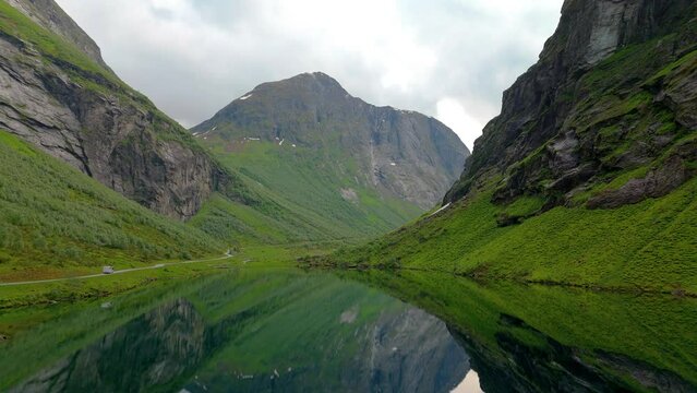 A serene video of a stunning lake in a valley, encircled by tall mountains. The tranquil scenery is enhanced by the mountains reflection in the lakes still water, Norweigan Fjords Stavbergvatnet Urke