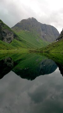 Norweigan Fjords Stavbergvatnet Urke, In the heart of a valley, a lake encircled by towering mountains, creating a serene and picturesque natural landscape with lush green grass and plants all around