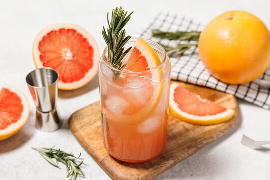 Grapefruit cocktail with rosemary garnish in a glass, served on a wooden cutting board. Vibrant, refreshing drink perfect for summer menu or cocktail recipes. Greyhound, lemonade, paloma, mocktail.