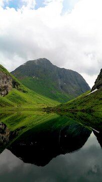 The tranquil image captures a mountain mirrored in a serene lake, encircled by vibrant greenery with mist shrouded peaks in the distance, Urke Norway