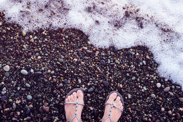 Women's feet on a pebble beach near the sea on a sunny day, toned. Vacation background	