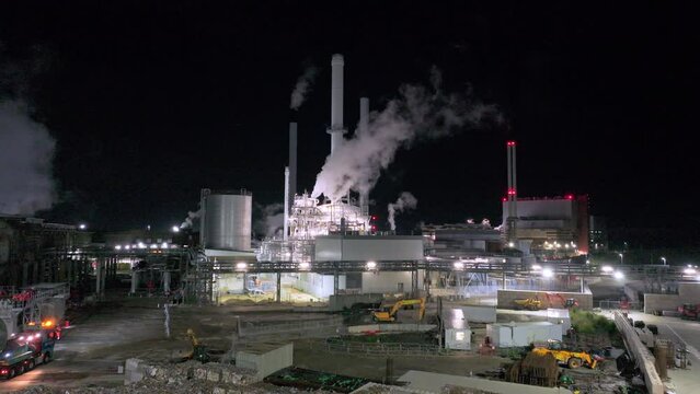 Aerial shot of paper mill industrial plant with pipes, machinery, chimneys and steam, at night.