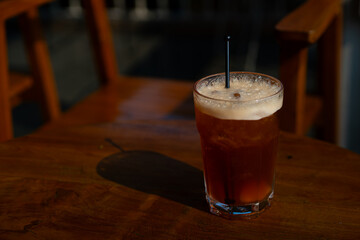 iced peach tea refreshment drink served on tall transparent glass, over wooden table surface, in cafe environment