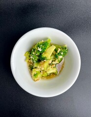 Healthy and crunchy stir fried broccoli with garlic dish. Oseng brokoli cah bawang putih on small white bowl. Food photography isolated on vertical dark black background from above top angle view.