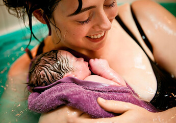 Water birth, a woman holding her newborn baby in her arms, joyful expression, labour in water.