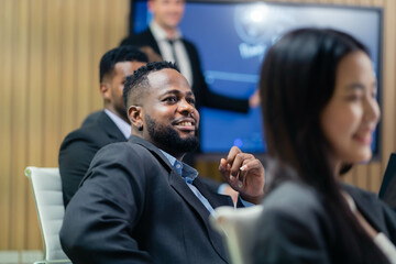 A man in a suit is smiling at a presentation. A woman is sitting next to him. The man is wearing a...