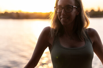 Self-steem woman in glasses by river at sunset, thoughtful expression