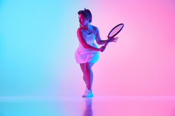 Skilled young woman, tennis player training in motion in neon light against vibrant gradient studio background. Concept of professional sport, championship, active lifestyle, tournament. Ad