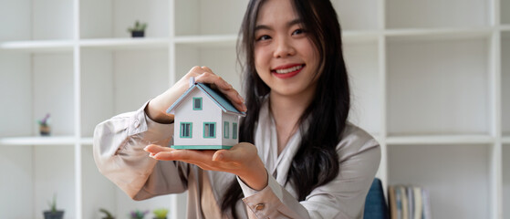 Smiling Woman Holding Miniature House Model in Hands, Real Estate Agent Promoting Property Sale,...