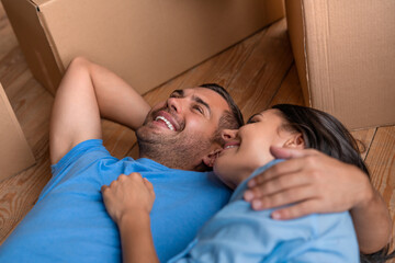 Young couple family in love hugging and resting lying on the floor among cardboard boxes at their new apartment house home, they just moved in. Daydreaming, making plans for the future.