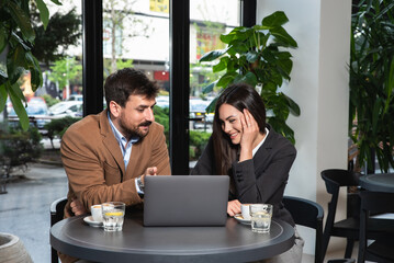 Two young colleagues businessman and businesswoman sitting at cafeteria working together on laptop. Teamwork of business people in coffee shop, brainstorming, work on company finance end economy.