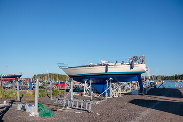 Yacht, sail boat ashore on support in a harbor boatyard for the winter storage and repair works before Launching, spring sunny weather, blue sky