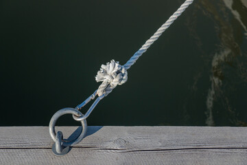 Mooring ring for boats in the port with carbine and black rope from the boat, wooden pier, sunny light, rope knot