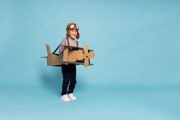 Asian little boy aviator playing and running with cardboard airplane isolated on blue sky...