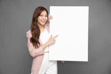 Naklejka premium Young Asian businesswoman showing and holding blank white billboard isolated on grey background