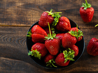 Fresh juicy strawberries in a bowl on a wooden table, top view