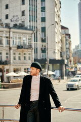 Red-haired man in debonair black coat and hat leaning on rail.