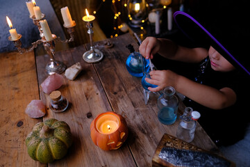 child makes magic out of focus, girl 3 years old in witch hat learns skill of magic at school of...