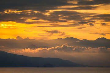 The photo captures a breathtaking golden sunset over majestic mountains. The sky is ablaze with hues of orange, pink, and gold, casting a warm glow on the rugged peaks. =