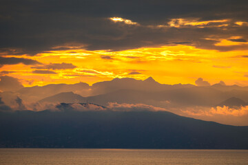 The photo captures a breathtaking golden sunset over majestic mountains. The sky is ablaze with hues of orange, pink, and gold, casting a warm glow on the rugged peaks. =