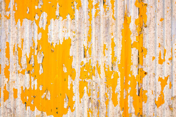 Close up of a weathered corrugated metal surface with peeling yellow paint, revealing rust and wear...
