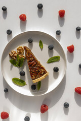 Pecan pie on a plate. Blueberries, nuts and mint leaves for dessert decoration. A yellow plate on a white background close-up.