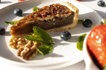 Pecan pie on a plate. Blueberries, nuts and mint leaves for dessert decoration. A yellow plate on a white background close-up.
