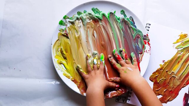 Child Finger Painting with Bright Colors. The video shows a child's hands mixing finger paint on a white surface. 