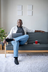 A man is sitting on a couch with a laptop on his lap