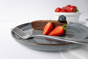 A piece of chocolate cake on a plate is decorated with berries. Dessert on a white background. Copy space, close-up.Fork on a plate
