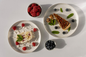 Plates with desserts close-up on a white background. Copy space. Pecan pie, meringue roll and chocolate cake are decorated with berries and mint leaves. Breakfast and tea