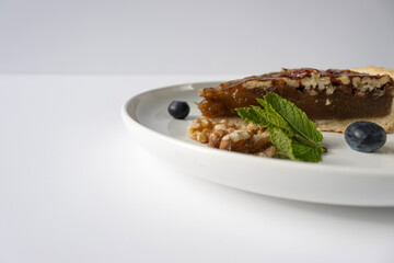 Pecan pie on a plate. Blueberries, nuts and mint leaves for dessert decoration. A yellow plate on a white background close-up.