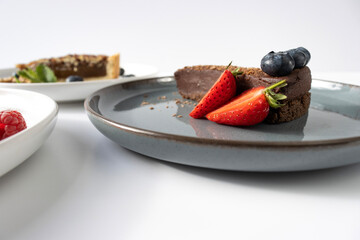 A piece of chocolate cake on a plate is decorated with berries. Dessert on a white background. Copy space, close-up.Fork on a plate