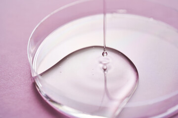 Serum or cosmetic oil flows into a transparent bowl on a purple background.
