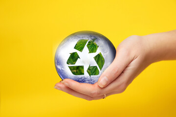 Female hand holding recycling arrows with the Earth planet on yellow background. Reuse Reduce Recycle. Earth day. Recycling sign created from leaves