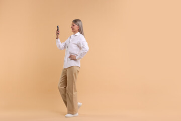 Senior woman with phone on beige background, space for text