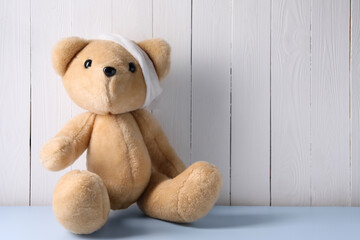 Toy bear with bandage on light blue table near white wooden wall, space for text