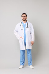 Full length portrait of smiling doctor on light grey background