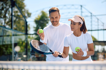 Athletic woman learning to serve the ball with help of paddle tennis coach.