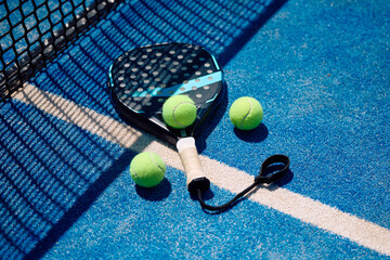 Paddle tennis racket and balls by the net on court.