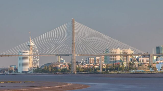Vasco da Gama Bridge over river Tagus timelapse in Lisbon with park of Nations district modern architecture, Portugal. View from newly opened walking route Percurso Ribeirinho de Loures
