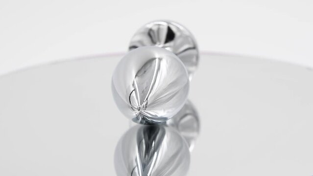 Close-up side view of metallic butt plug with pink round shaped crystal spinning on mirror surface against white background. Soft focus. Real time video. Adult sex toys theme.