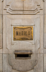 A bronze plate on a marble wall with the wording "Madrid" outside the post office in Seville, Spain
