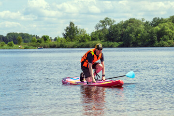 A man is floating on the river balancing on a board, paddling along the river.