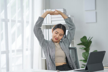 Woman stretching her arms at a desk with a laptop in a bright office, taking a break from work to...