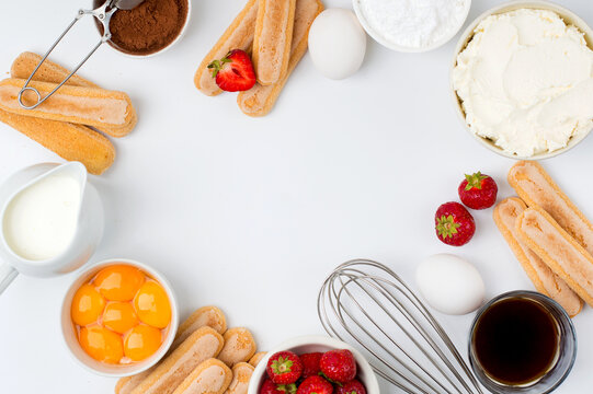 Ingredients for preparing the Italian dessert tiramisu with strawberries. Savoiardi cookies, mascarpone, yolks, strawberries, cream and cocoa on a light background, top view.Free space for copying.